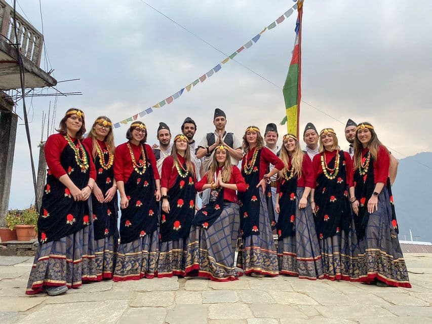 Un grupo de WeRoad con atuendos tradicionales rojos y negros posa para una foto en una terraza de piedra bajo banderas de oración.