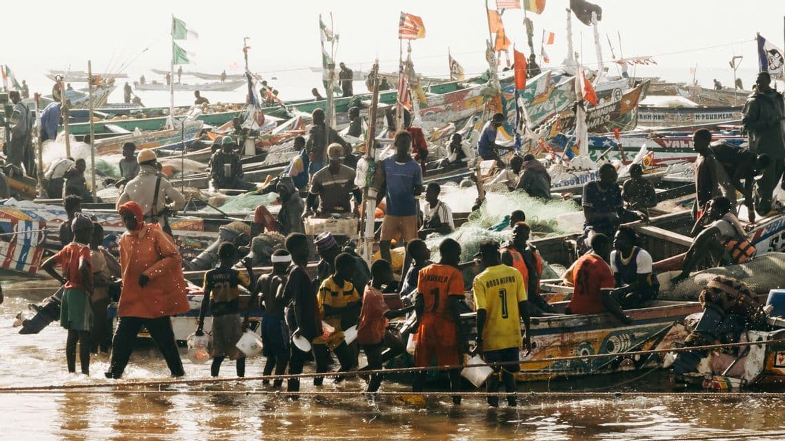 Un gran grupo de pescadores trabajando en y alrededor de docenas de coloridas embarcaciones tradicionales apiñadas en aguas poco profundas.