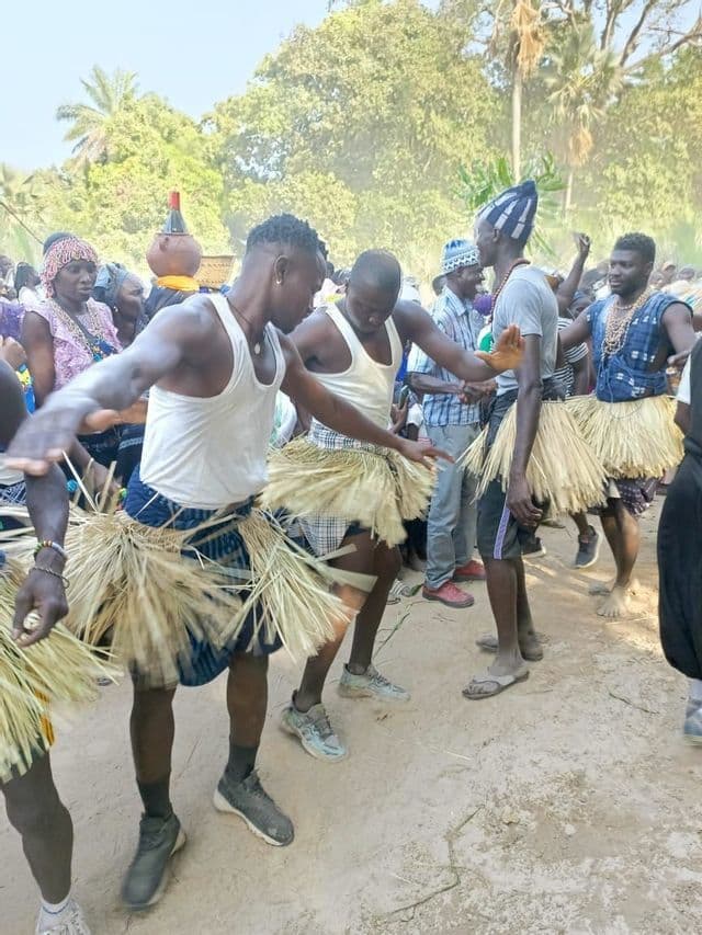 Un grupo de hombres con faldas de hierba tradicionales, sobre ropa moderna, bailan juntos durante una ceremonia cultural al aire libre.