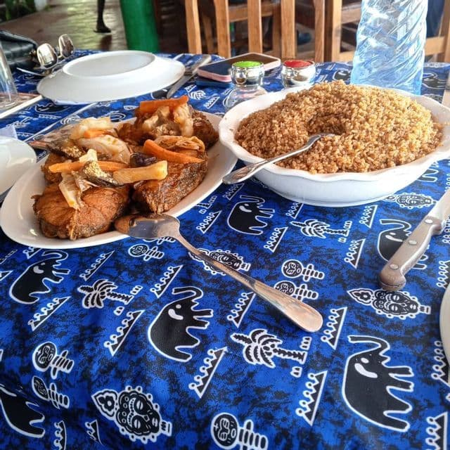 Una bandeja de pescado frito con verduras y un cuenco de grano servido sobre un mantel azul con motivos étnicos.
