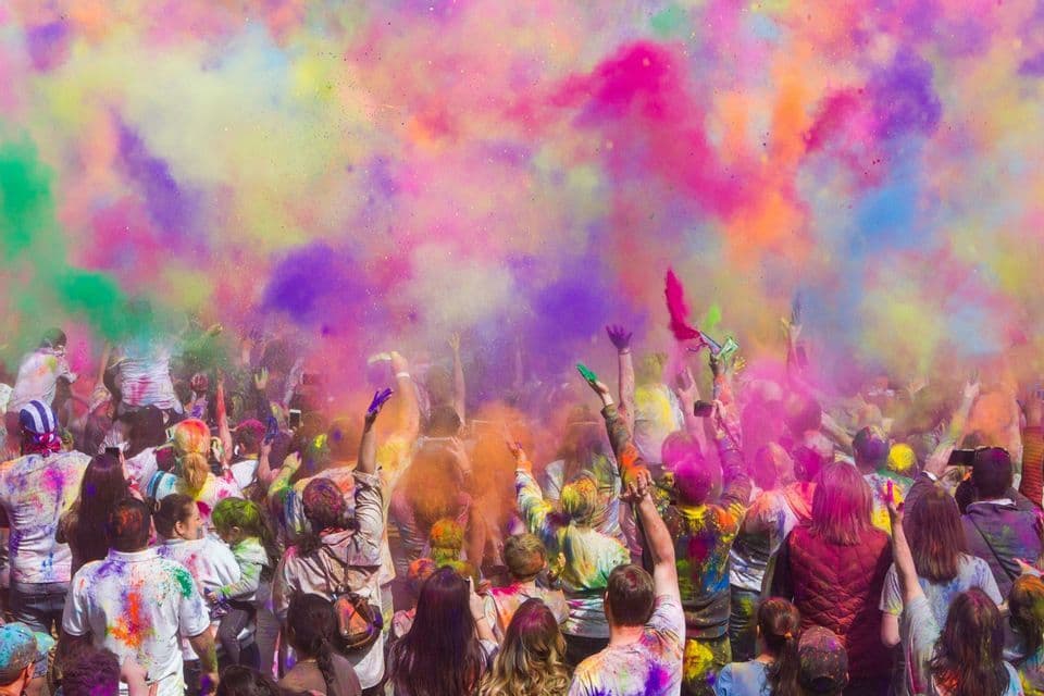 Un viaje en grupo de WeRoad visto desde atrás, lanzando polvos de colores como rosa y morado al aire durante un festival.