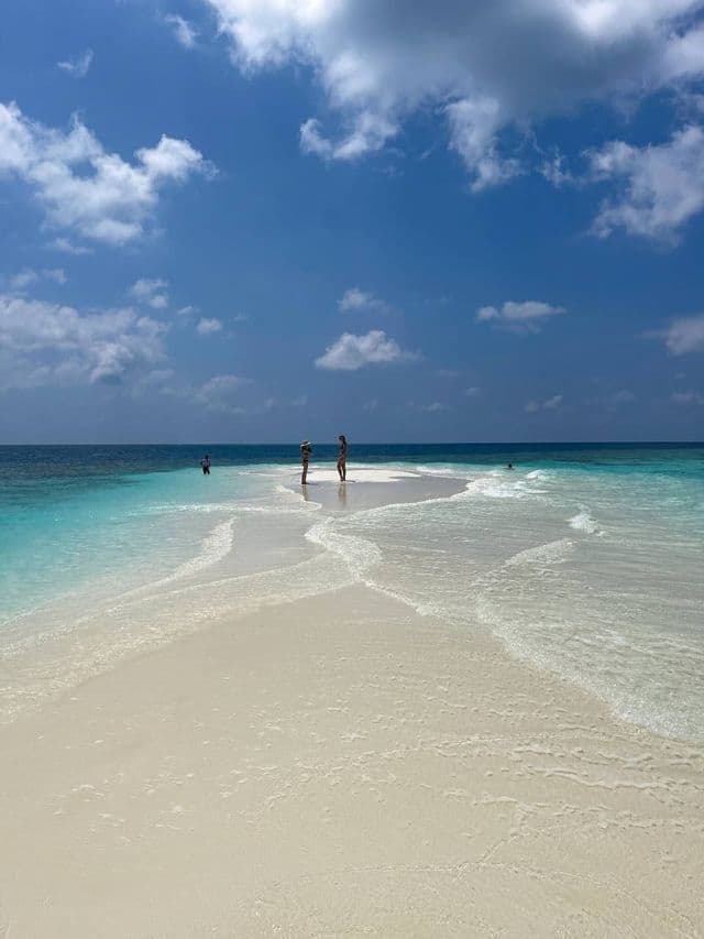 Eine WeRoad Gruppenreise steht auf einer weißen Sandbank, umgeben von türkisfarbenem Wasser unter blauem Himmel mit Wolken.