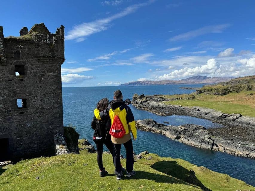Deux personnes lors d'un voyage de groupe WeRoad se tiennent sur une falaise herbeuse à côté d'une ruine en pierre, regardant la mer et le littoral rocheux.