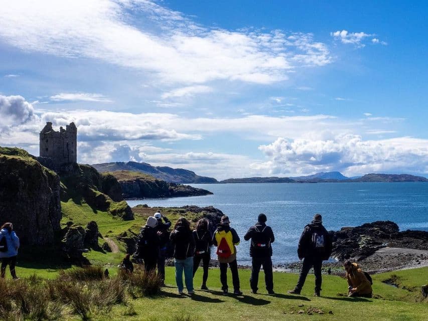 Un groupe WeRoad se tient sur une côte herbeuse, contemplant les ruines d'un château sur une falaise surplombant la mer.