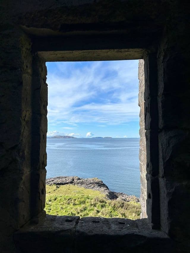Une vue sur la mer, une côte verdoyante et des îles lointaines vues de l'intérieur à travers une fenêtre en pierre.