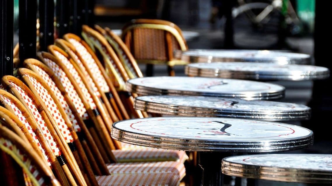 Una fila di sedie da bistrò in vimini con motivi rossi e bianchi accanto a tavoli rotondi in metallo in un caffè all'aperto.