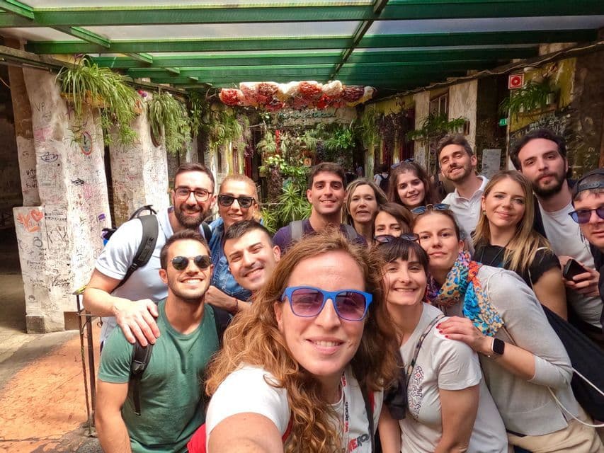 Eine lächelnde WeRoad-Gruppenreise posiert für ein Selfie in einem engen, mit Hängepflanzen und Graffiti geschmückten Innenhof.