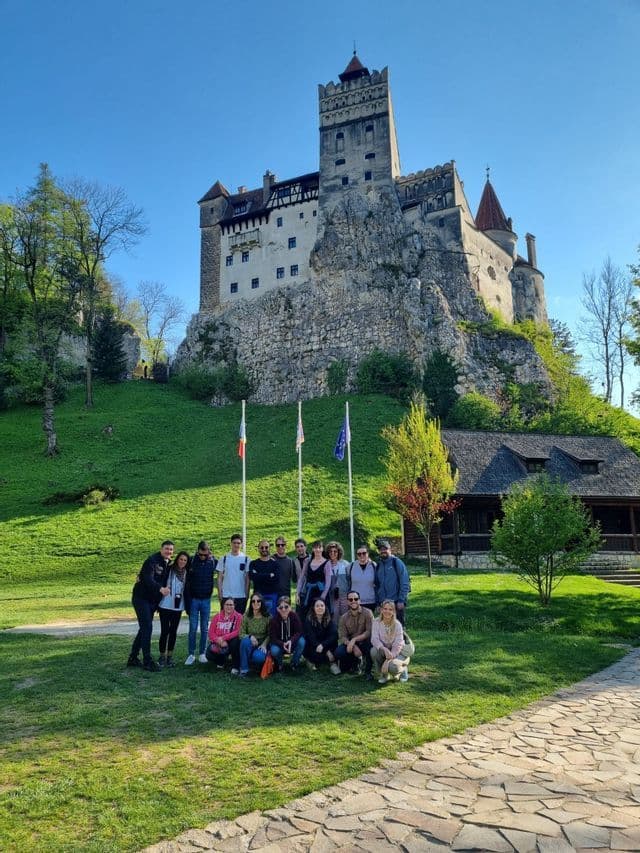 Eine WeRoad-Gruppe posiert an einem sonnigen Tag vor einer historischen Burg, die auf einem felsigen grünen Hügel thront.
