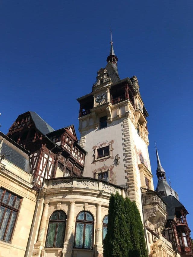 Eine Untersicht auf den kunstvollen Uhrenturm eines Schlosses mit Türmchen und Fachwerkarchitektur vor strahlend blauem Himmel.