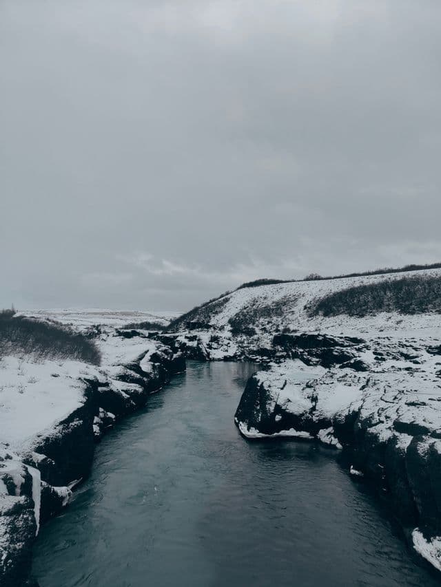 Un fiume scorre attraverso un canyon roccioso e innevato in una giornata nuvolosa.