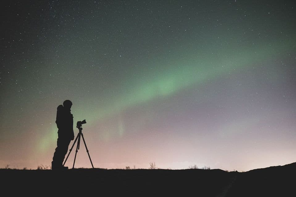 Silhouette di un fotografo con la macchina fotografica su treppiede che osserva l'aurora boreale sotto un cielo stellato