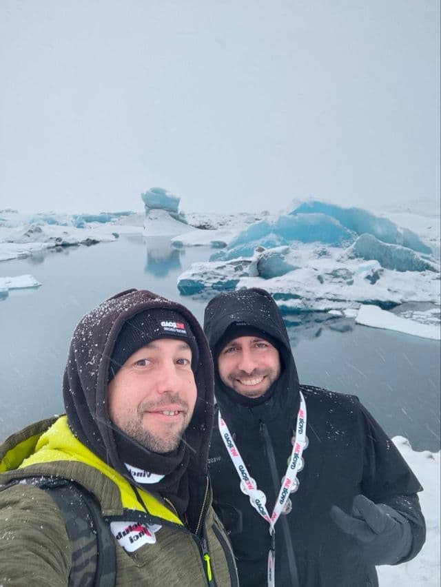 Due partecipanti di un viaggio di gruppo WeRoad si fanno un selfie in un paesaggio innevato con iceberg blu che galleggiano in una laguna.