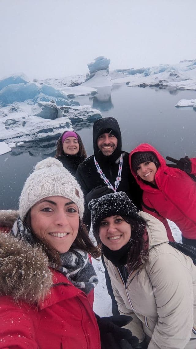 Un viaggio di gruppo WeRoad scatta un selfie durante una nevicata, con una laguna glaciale e iceberg sullo sfondo.