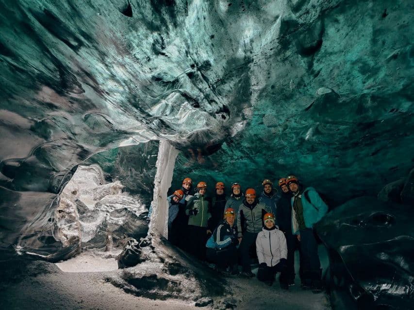 Un gruppo WeRoad con caschi e lampade frontali posa per una foto di gruppo all'interno di una grande grotta di ghiaccio con pareti turchesi.