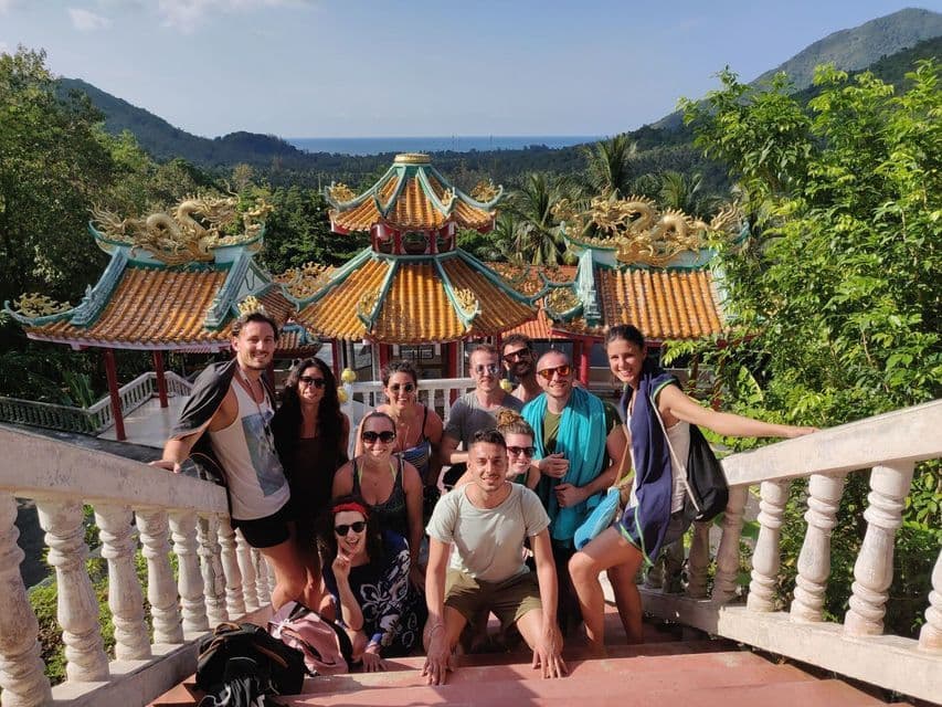 Un voyage en groupe WeRoad posant pour une photo sur les marches d'un temple traditionnel avec des dragons dorés et une vue sur la mer.