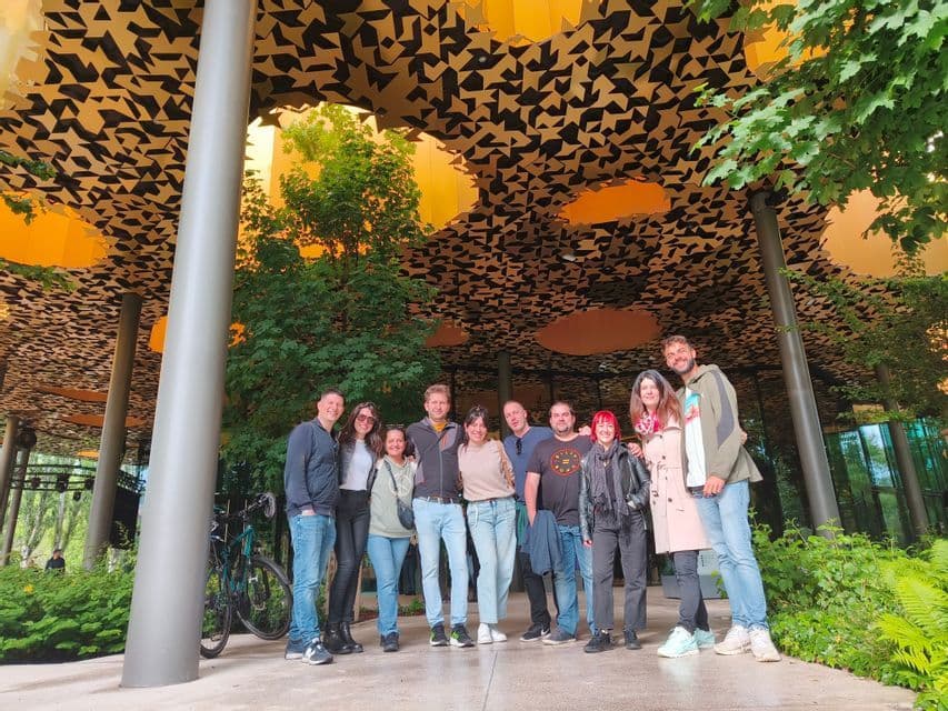 Un viaje en grupo de WeRoad posando juntos bajo un edificio moderno con un techo con diseño dorado y negro, rodeados de árboles.