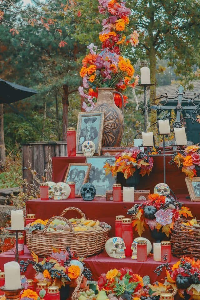 Un altar de Día de Muertos de varios niveles decorado con flores coloridas, calaveras pintadas, velas, fruta y fotografías.