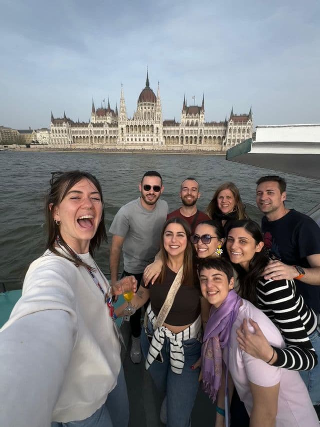 Un grupo de WeRoad se toma una selfie en un barco, con un edificio del parlamento ornamentado visible al otro lado del río.