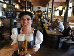 Una cameriera in un tradizionale dirndl sorride mentre tiene due grandi boccali di birra in un pub rustico.