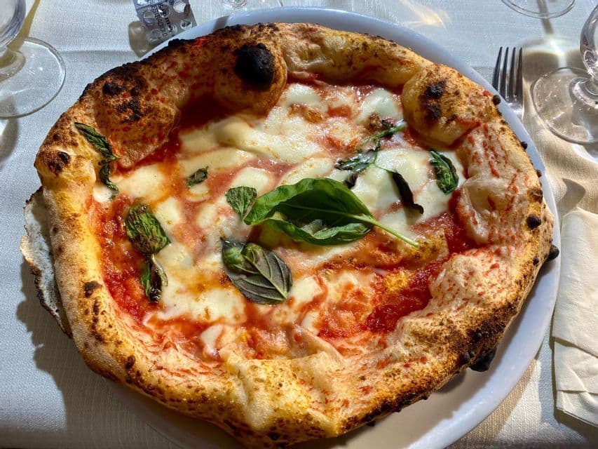 Eine neapolitanische Pizza Margherita mit verkohltem Rand, geschmolzenem Mozzarella und frischem Basilikum auf einem weißen Teller.