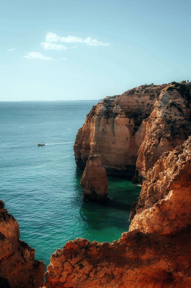 Una barca naviga su acqua turchese accanto a grandi scogliere arancioni sotto un cielo limpido.
