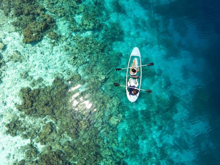 Vista aerea di due persone che remano in un kayak trasparente su una barriera corallina in acqua cristallina turchese.