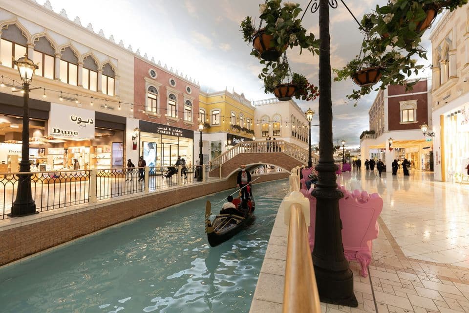 Una gondola con un gondoliere naviga lungo un canale interno all'interno di un centro commerciale progettato con architettura in stile veneziano e un cielo dipinto.