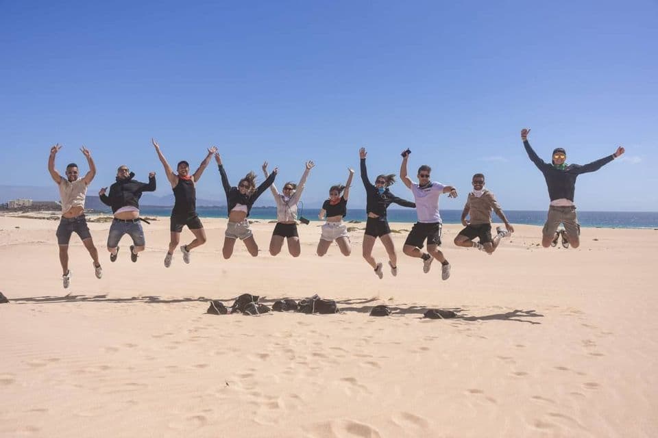 Un viaggio di gruppo WeRoad con nove persone che saltano su una spiaggia sabbiosa, con l'oceano sullo sfondo.