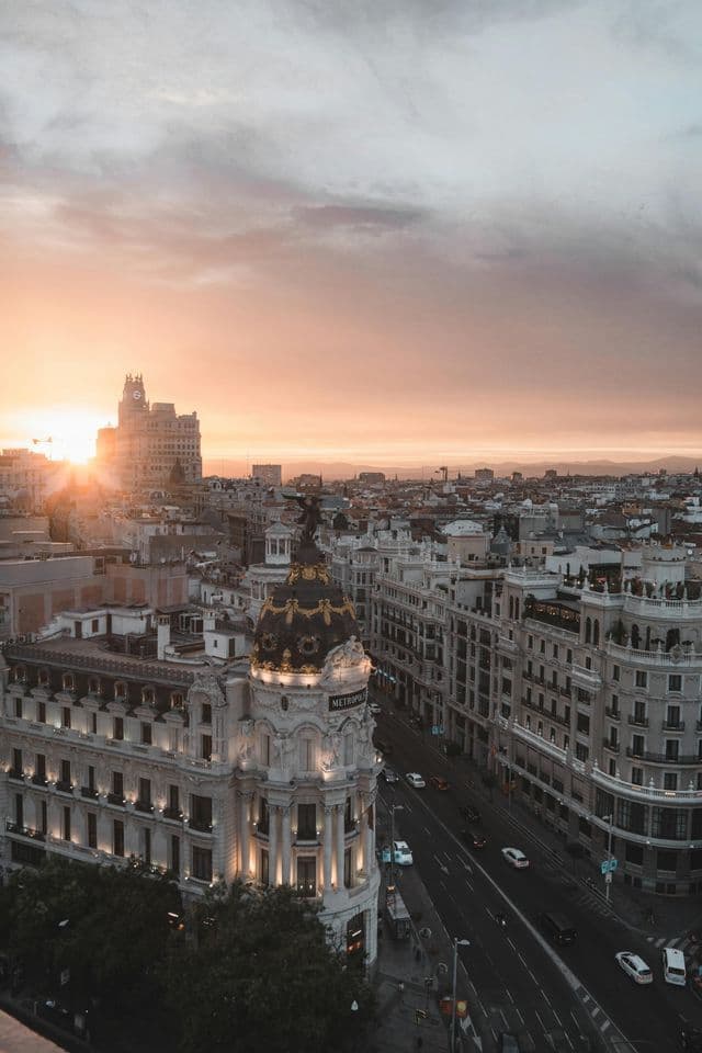 Vista elevata sull'architettura densa di una città, con il sole che tramonta dietro gli edifici e illumina il cielo con un bagliore arancione.
