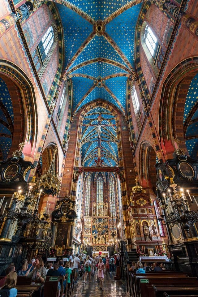 Vista en contrapicado del interior de una catedral ornamentada con una bóveda azul estrellada y visitantes.