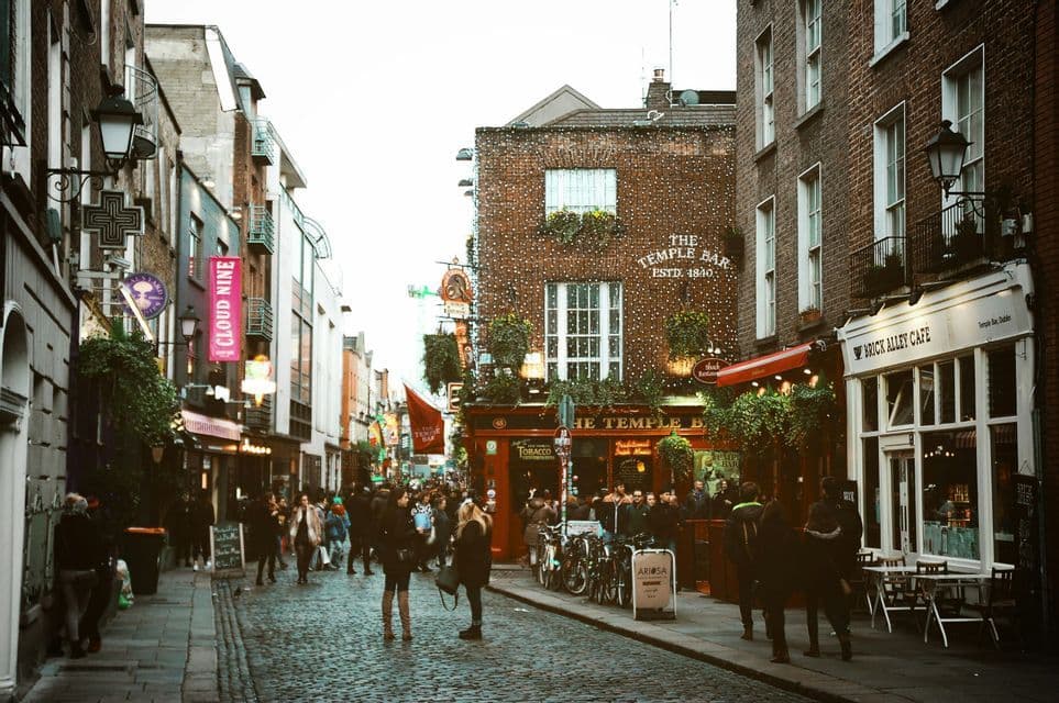 Una folla di persone su una strada di ciottoli di fronte a The Temple Bar, un pub storico in mattoni decorato con luci.