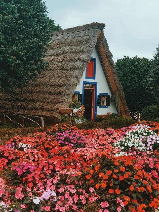 Un tradizionale cottage a capanna con tetto di paglia e finiture colorate si trova dietro un'aiuola di fiori variopinti.