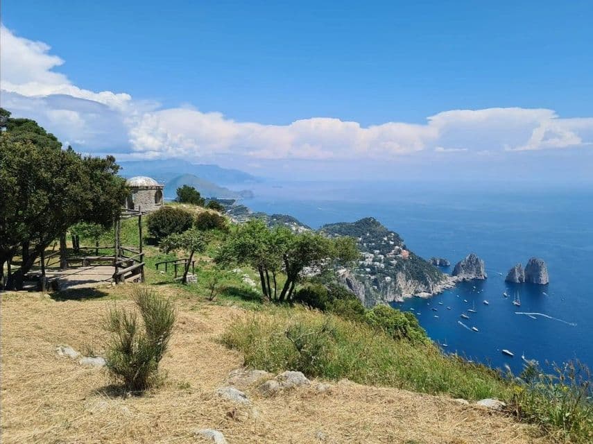Una vista panoramica dall'alto da una scogliera erbosa, che abbraccia una città costiera, formazioni rocciose suggestive e imbarcazioni sparse nell'azzurro profondo del mare.