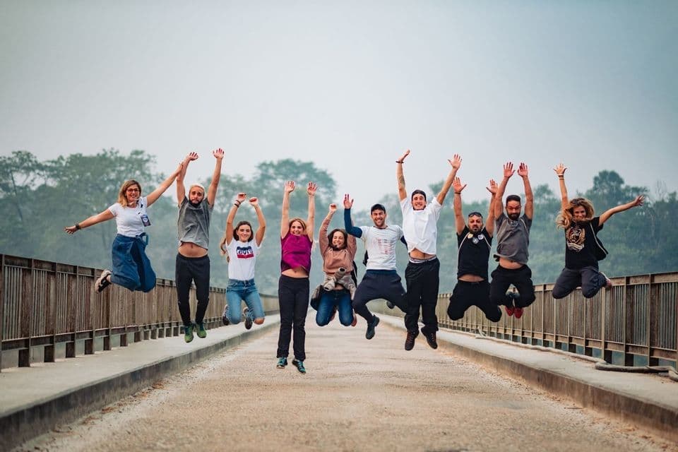 A WeRoad group trip of nine people jumping together in the air with their arms raised on a long bridge.