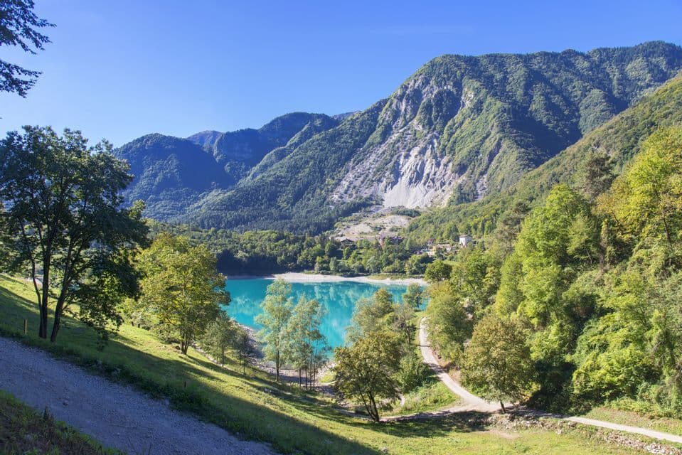 Un lago turchese vibrante si trova in una valle circondata da montagne verdi e boscose sotto un cielo azzurro e limpido.
