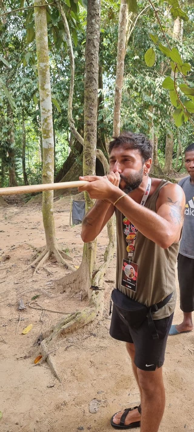 Un uomo in un viaggio di gruppo WeRoad prova l'uso di una cerbottana tradizionale nella foresta.