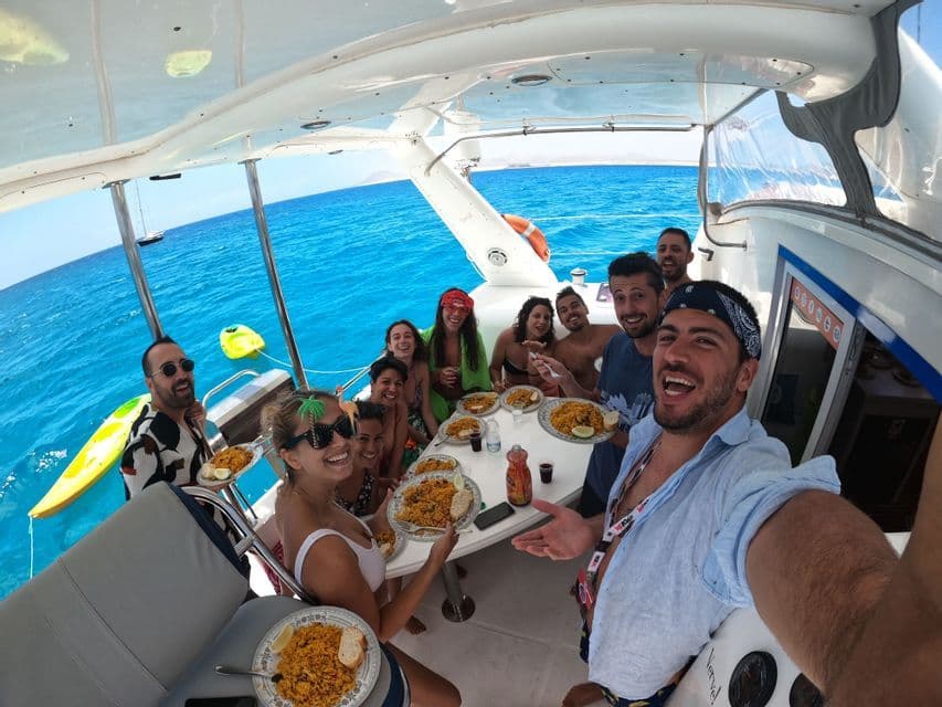 Eine lächelnde WeRoad-Gruppe macht ein Selfie beim gemeinsamen Mittagessen auf einem Katamaran auf dem strahlend blauen Meer.