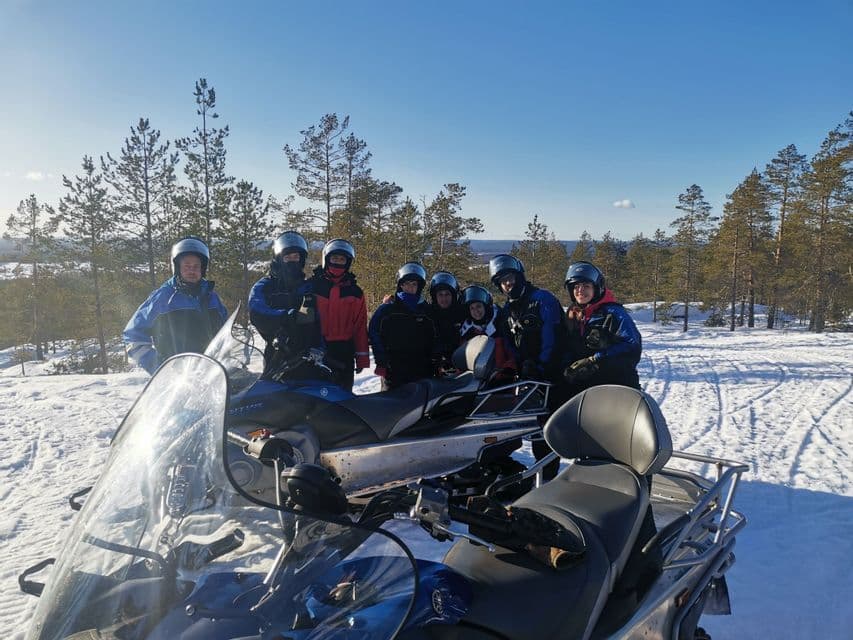 Eine WeRoad-Gruppe mit Helmen posiert für ein Foto neben Schneemobilen in einer verschneiten Landschaft mit Kiefern.