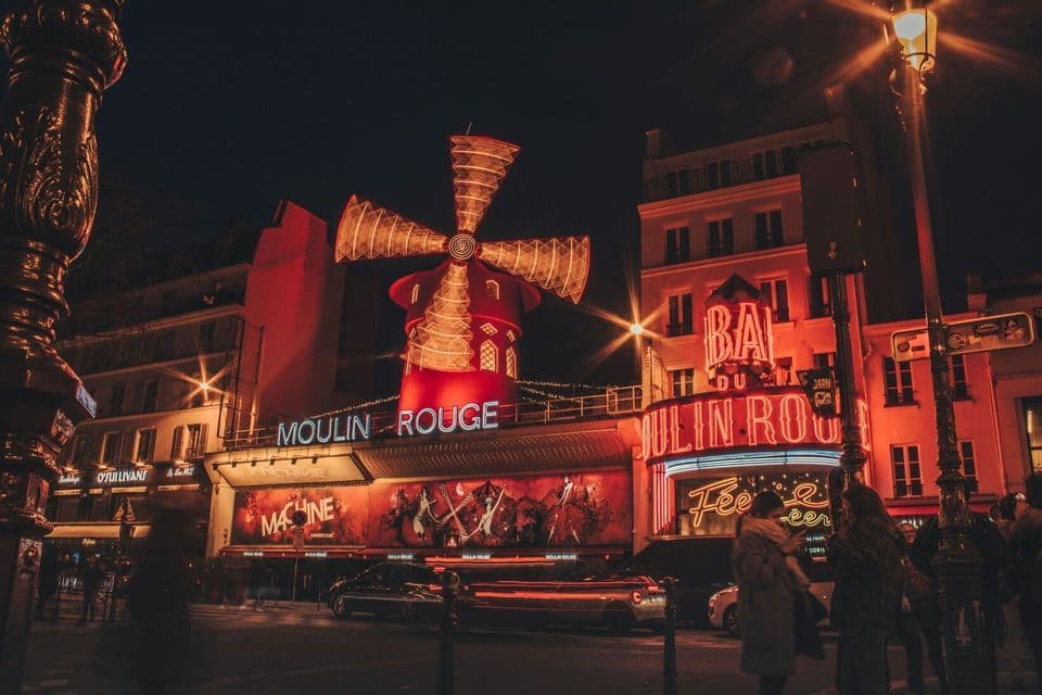 The facade of the Moulin Rouge at night, its iconic red windmill and signs glowing with bright red neon lights.