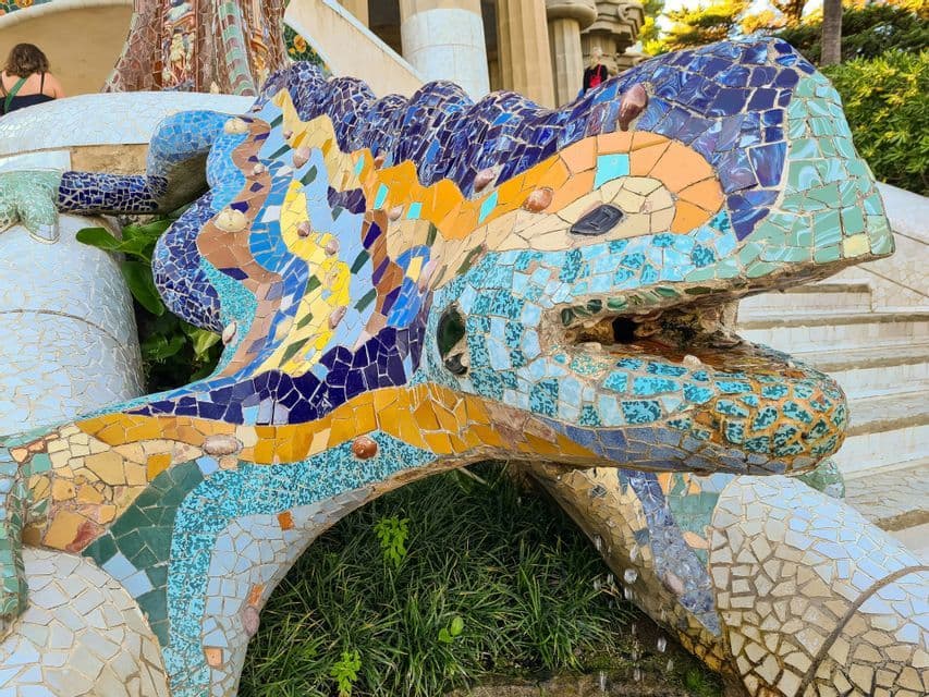 Primo piano di una scultura di lucertola a mosaico colorata con acqua che cola dalla bocca su una scala esterna.