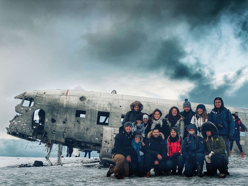 Un viaje en grupo de WeRoad con ropa de invierno posando para una foto frente a un avión estrellado en un paisaje nevado.