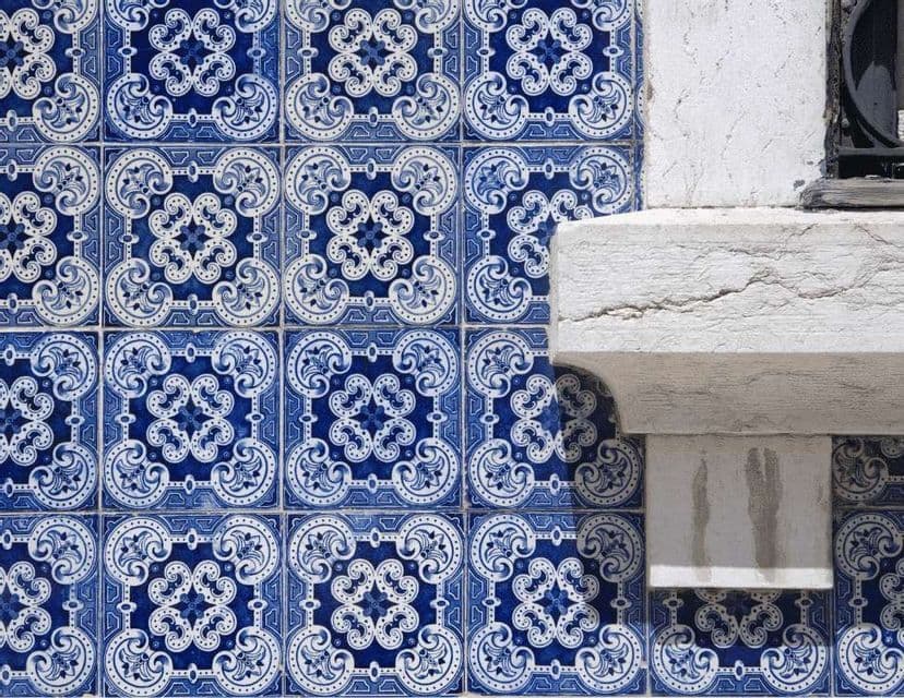 Primo piano di una parete rivestita con piastrelle blu e bianche a motivi floreali, accanto a un davanzale in pietra bianca.