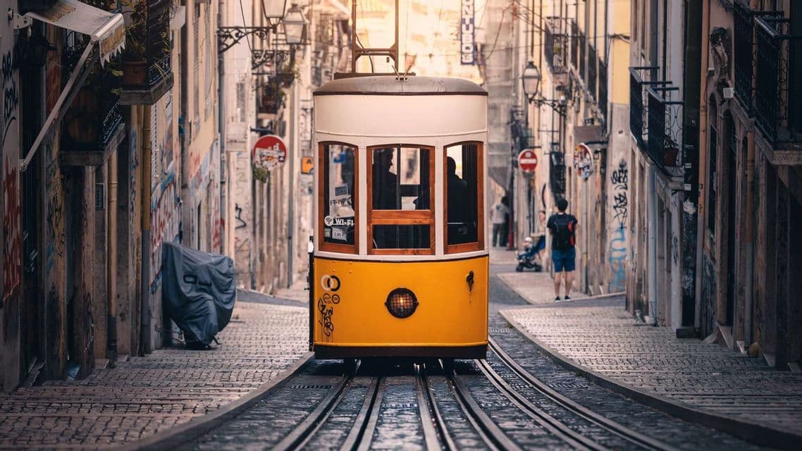 Un tram giallo e bianco sui binari sale una ripida e stretta strada acciottolata, affiancata da edifici.