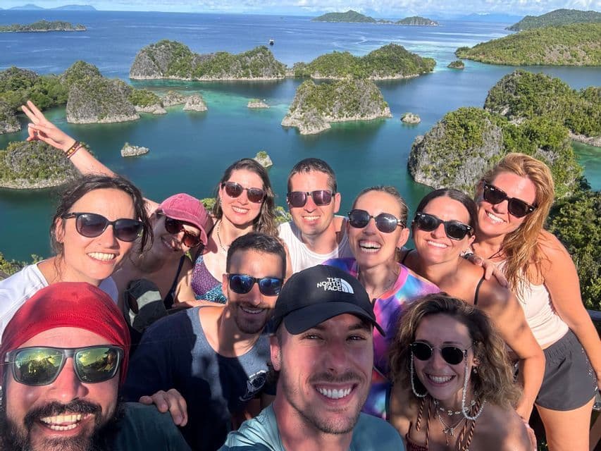 Un grupo de WeRoad se toma una selfie sonriente desde un mirador elevado con vistas a una bahía de islas rocosas, verdes y aguas turquesas.