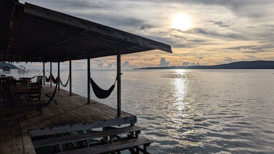 Una terraza de madera con hamacas con vistas al mar al atardecer bajo un cielo nublado.