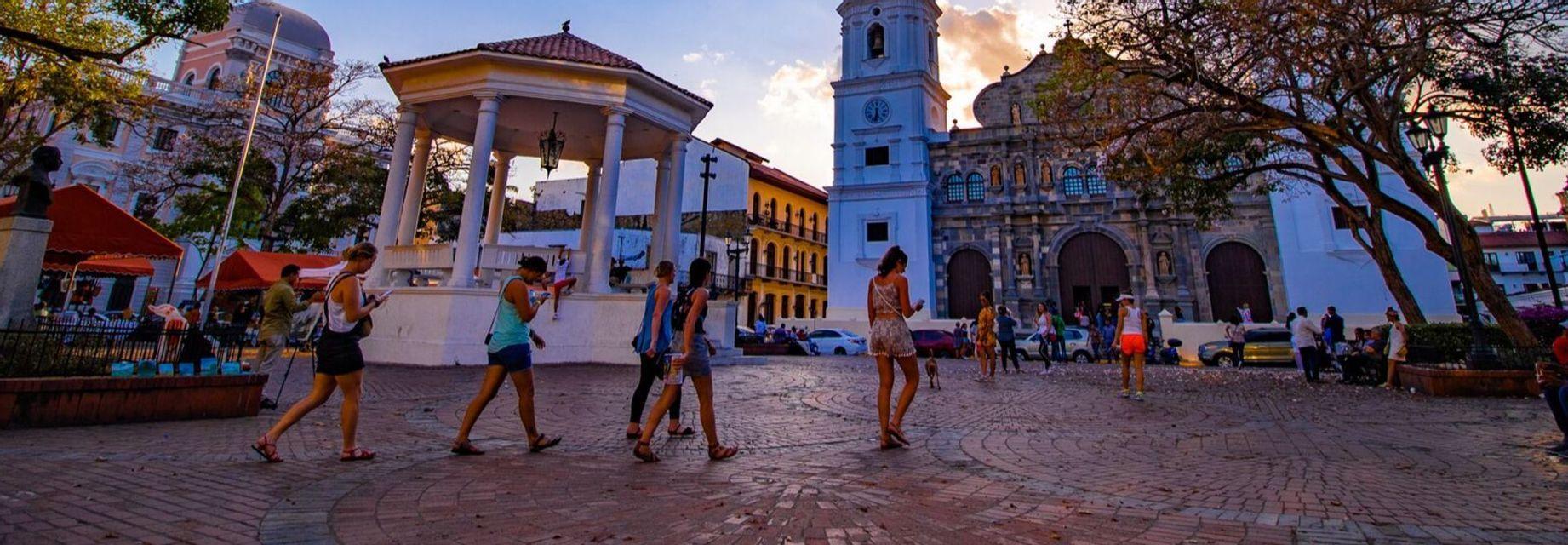 Un viaggio di gruppo WeRoad attraversa una piazza acciottolata con un gazebo e una chiesa coloniale al tramonto.