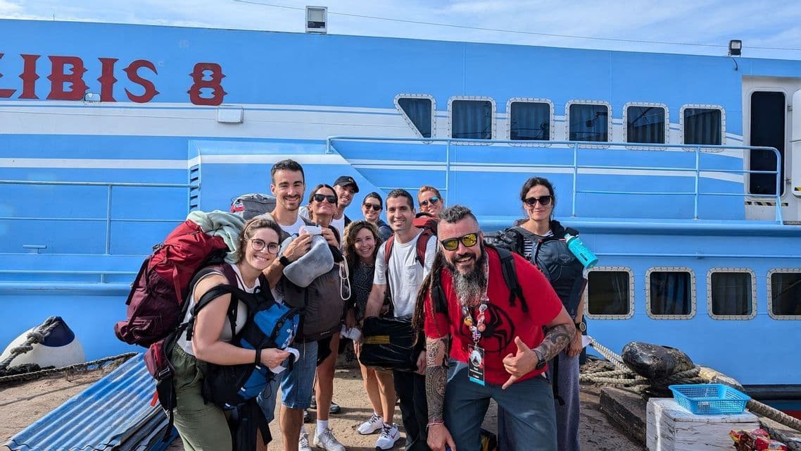 Un grupo de WeRoad con mochilas posa para una foto en un muelle frente a un gran ferry azul.