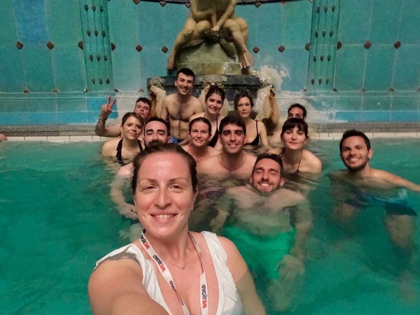 Un groupe WeRoad prend un selfie en se détendant dans une piscine thermale intérieure ornée d'une fontaine.
