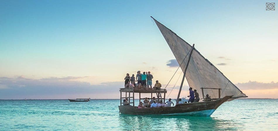 Eine WeRoad Gruppenreise segelt bei Sonnenuntergang auf einem traditionellen hölzernen Dhau-Boot auf ruhigem, türkisfarbenem Wasser.
