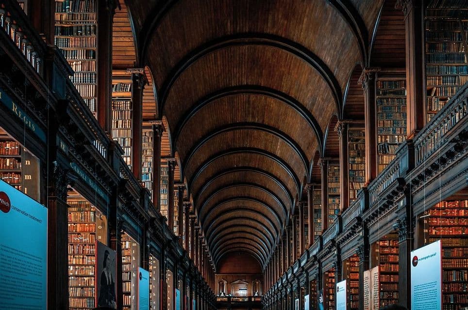 The long hall of a historic library with a high, arched wooden ceiling and walls lined with towering bookshelves.
